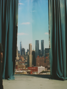 A set of theater curtains pulling back to reveal a city skyline, symbolizing the interconnectedness of live performance and urban life