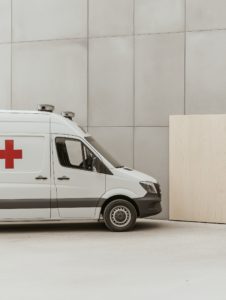 An ambulance parked outside a gym with a for sale sign, representing the decline in emergency services