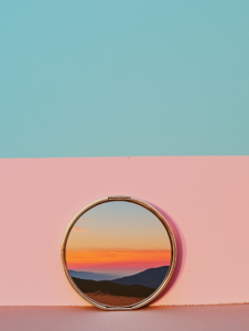 A makeup compact opening to reveal a sunset, symbolizing the vibrancy and color palettes that beauty brings to personal expression