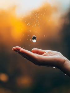 A single drop of rain falling into an open hand, representing the nourishing effect of faith on the soul