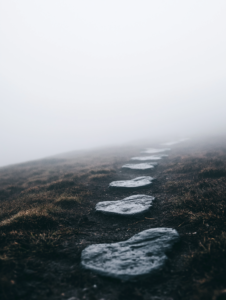 A trail of footprints leading into a dense fog, with glimpses of exciting discoveries just beyond view