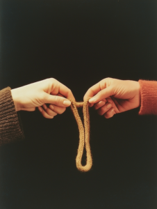 Two hands knitting a single scarf together, symbolizing the warmth created through mutual efforts in a close bond