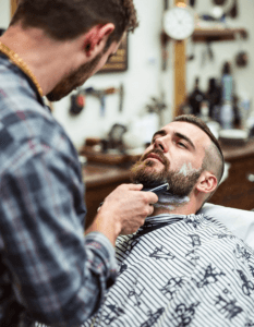 A barber giving a classic shave with a straight razor, surrounded by vintage décor and grooming tools