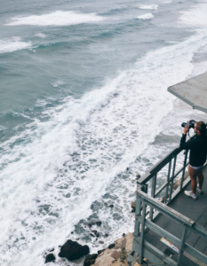 A lifeguard standing atop a watchtower, scanning the ocean with binoculars as waves crash on the shore below